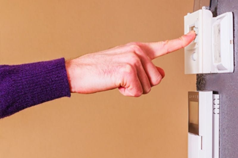 A person presses a thermostat. Heat Pump Versus Furnace.