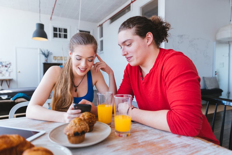 Young couple using phone to check social media feed over breakfast.