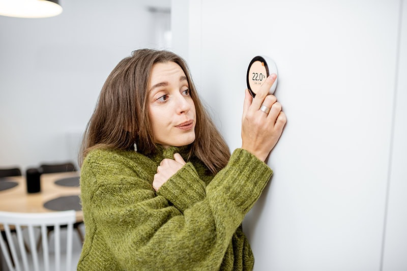 Why Is My Heat Pump Turning On and Off Frequently? A girl turning the thermostat up.