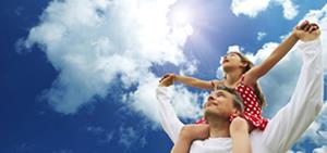 Father holding daughter on shoulders as they look at the blue sky and clouds passing by.
